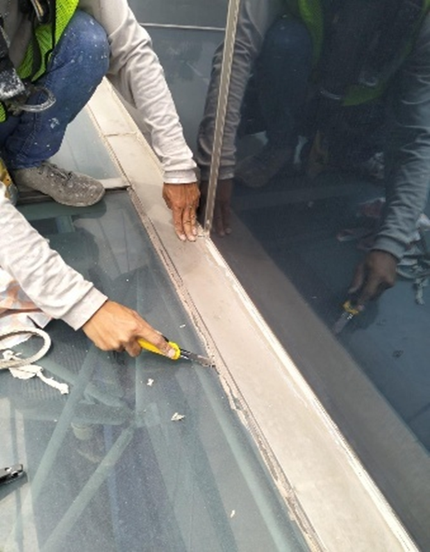 Rope access technician applying structural sealant to foyer joint